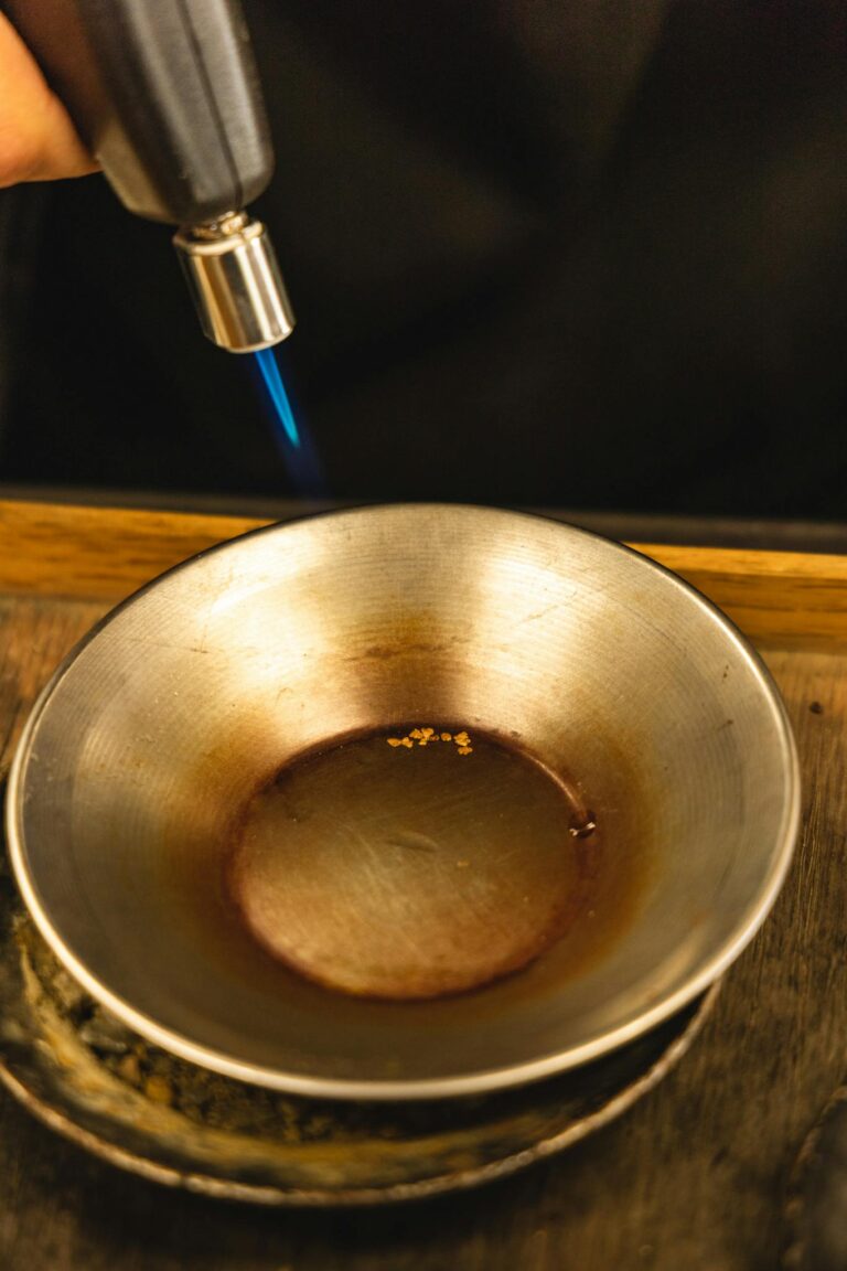 A blowtorch melting gold inside a metal bowl, showcasing intense heat and craftsmanship.