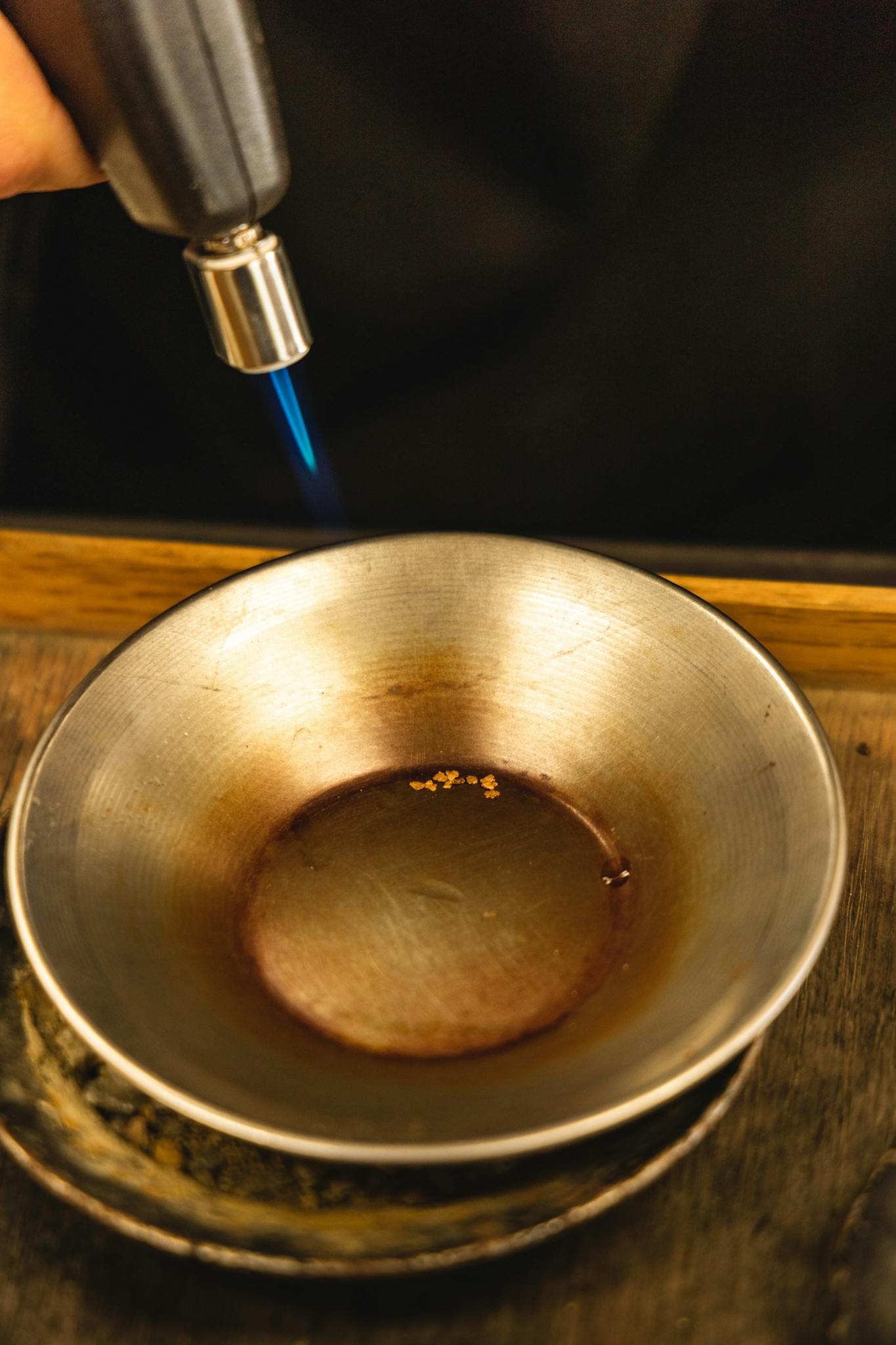 A blowtorch melting gold inside a metal bowl, showcasing intense heat and craftsmanship.