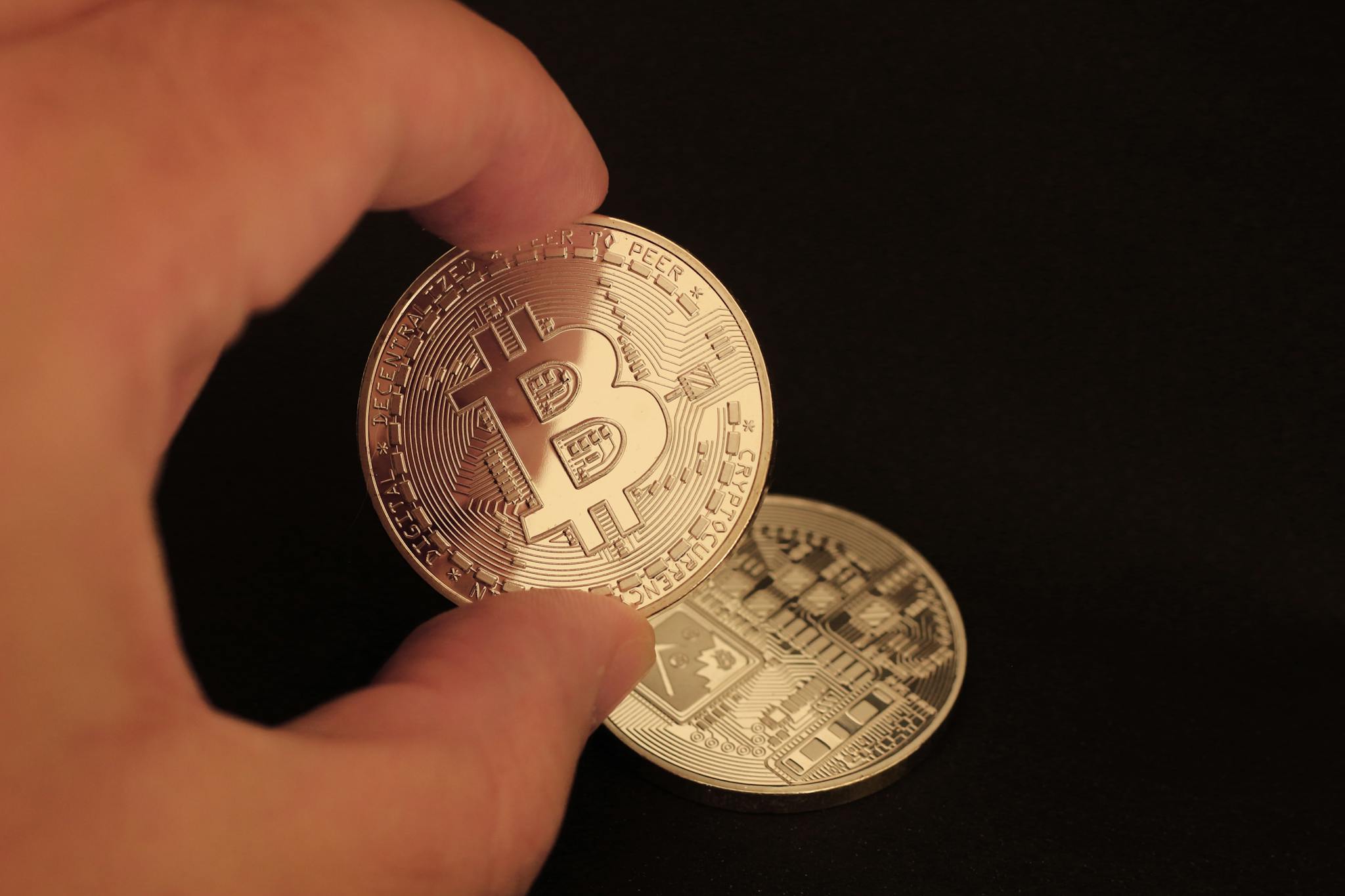 Close-up of a hand holding a Bitcoin coin on a dark background.